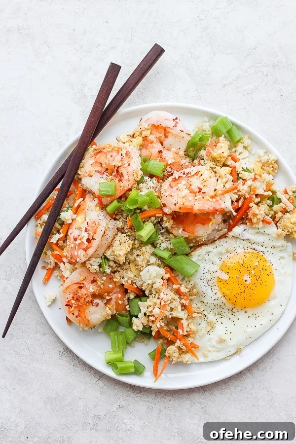 Shrimp Fried Cauliflower Rice - for when you are craving take-out, but also want to eat clean! (Paleo + Whole30 + Gluten-Free) #whole30recipes #shrimpfriedcauliflowerrice #paleorecipes #easyweeknightdinners Shrimp fried cauliflower rice on a white plate.