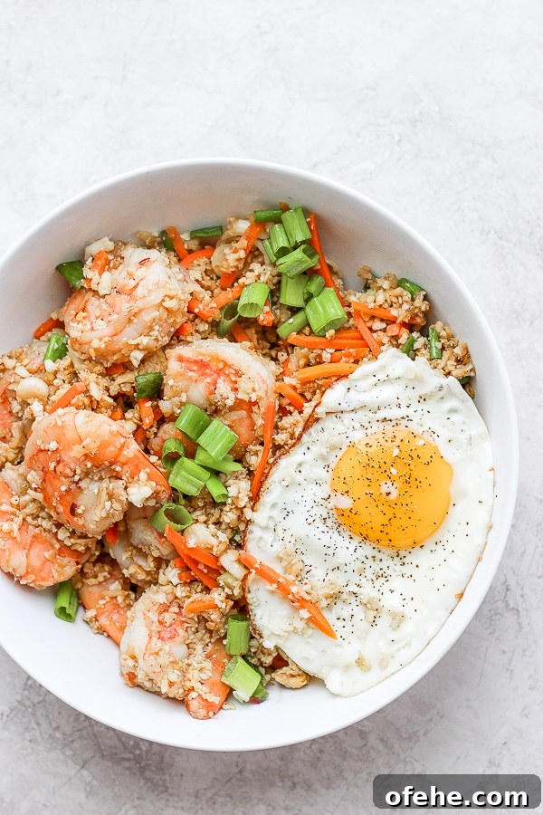 Shrimp Fried Cauliflower Rice - for when you are craving take-out, but also want to eat clean! (Paleo + Whole30 + Gluten-Free) #whole30recipes #shrimpfriedcauliflowerrice #paleorecipes #easyweeknightdinners Shrimp fried cauliflower rice in a bowl with a fried egg on top.