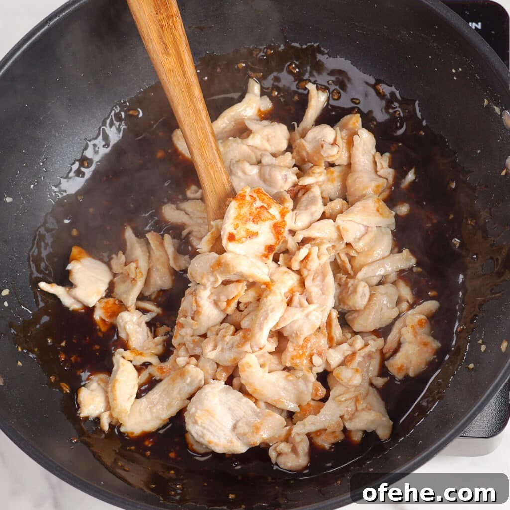 Garlic Chicken with Broccoli Stir-Fry Recipe 8 Chicken being mixed into sauce with wooden spoon in a large wok