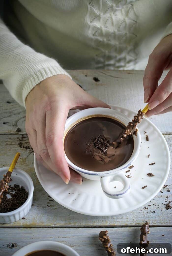 A hand holding the mug of hot chocolate and dipping chocolate stick.