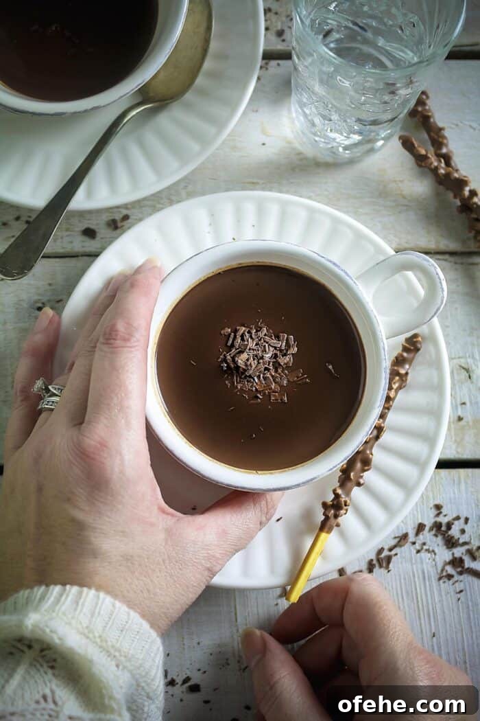 White cups with hot cocoa and saucers on a white wooden surface.