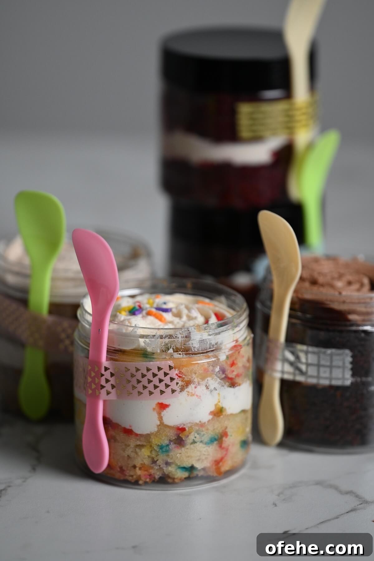 close up view of plastic jars with cake in the jar including funfetti and chocolate with attached sample spoons.