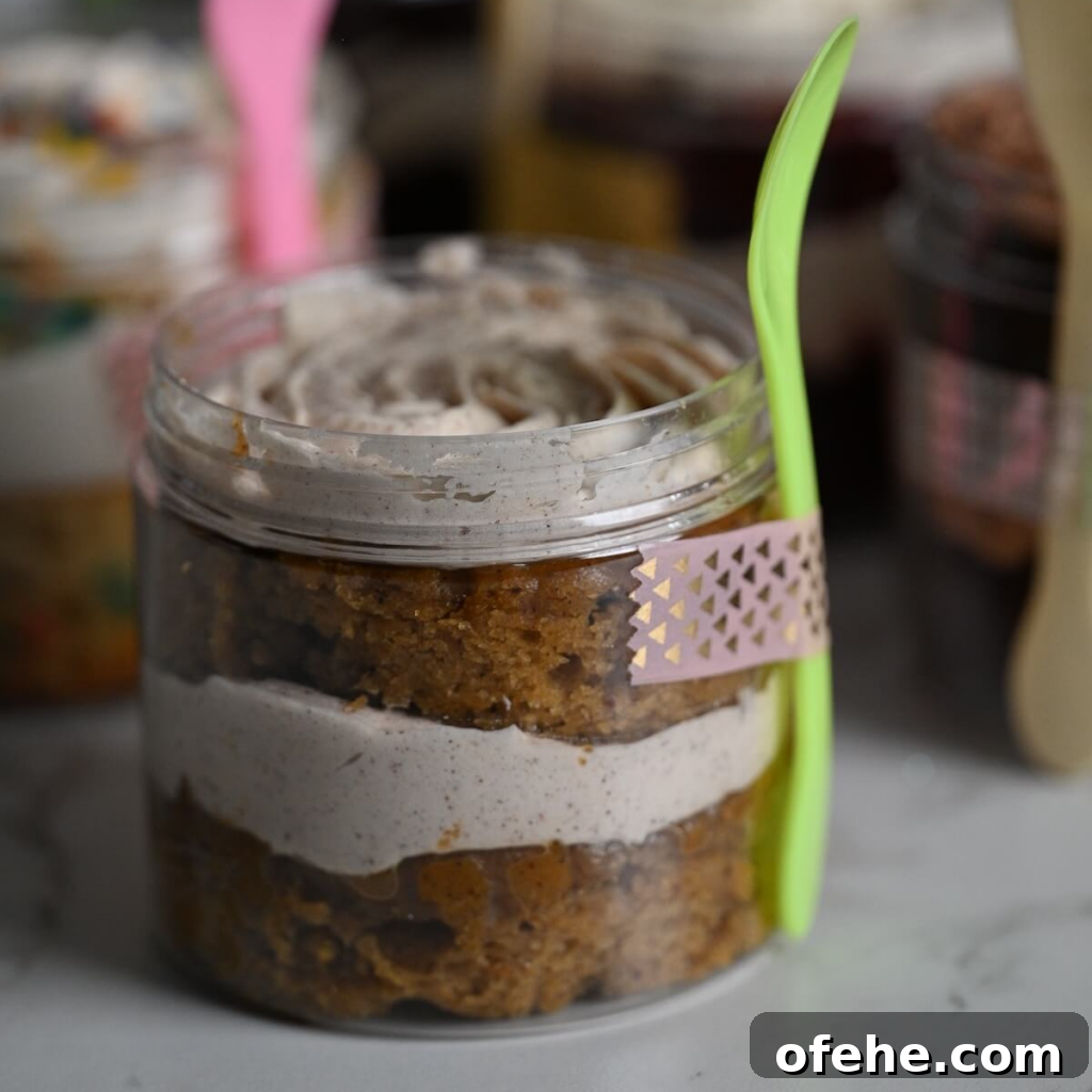 close up view of a plastic jar with layers of moist carrot cake and cinnamon buttercream with a spoon and washi tape attached to the jar.