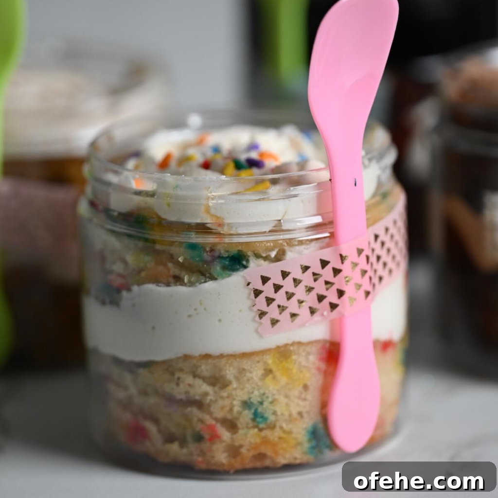 close up view of a plastic jar with funfetti cake, vanilla frosting, and rainbow sprinkles ready to serve.
