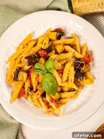 Pasta with eggplant and cherry tomatoes in a bowl garnished with fresh basil.