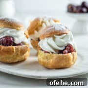 Three Windbeutel with cherry sauce and whipped cream on a dessert plate.
