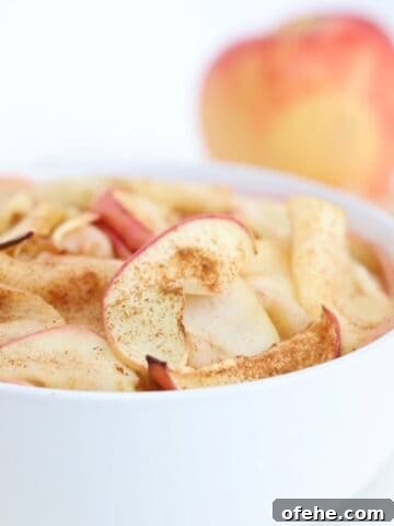 Air fried apple slices in a white bowl with an apple in the background.