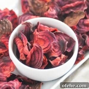 Crispy Air Fryer Beet Chips Recipe 9 Beet chips in a white bowl on a white platter with more beet chips.