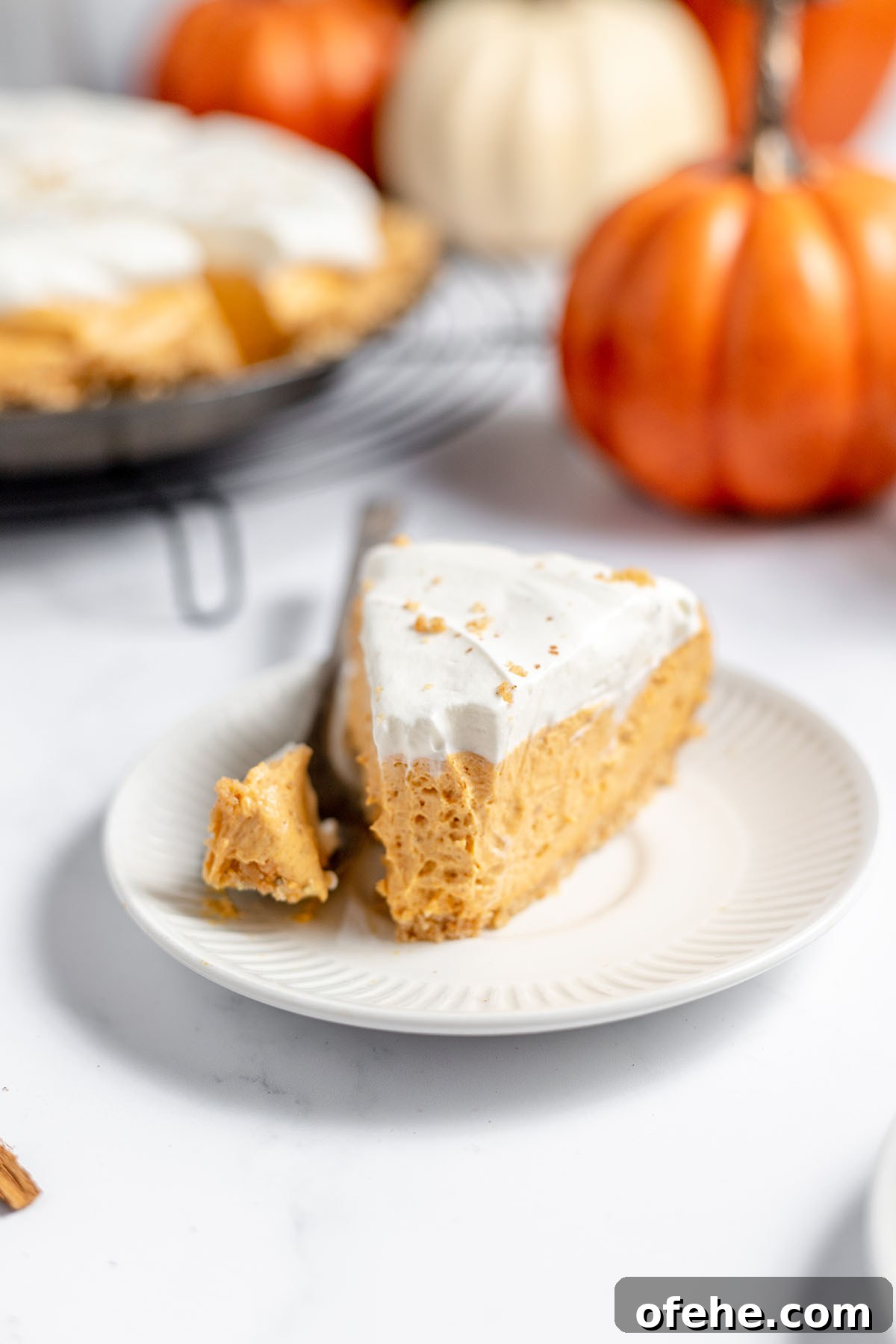 A slice of Pumpkin Cheesecake on a white plate with a bite on a fork.