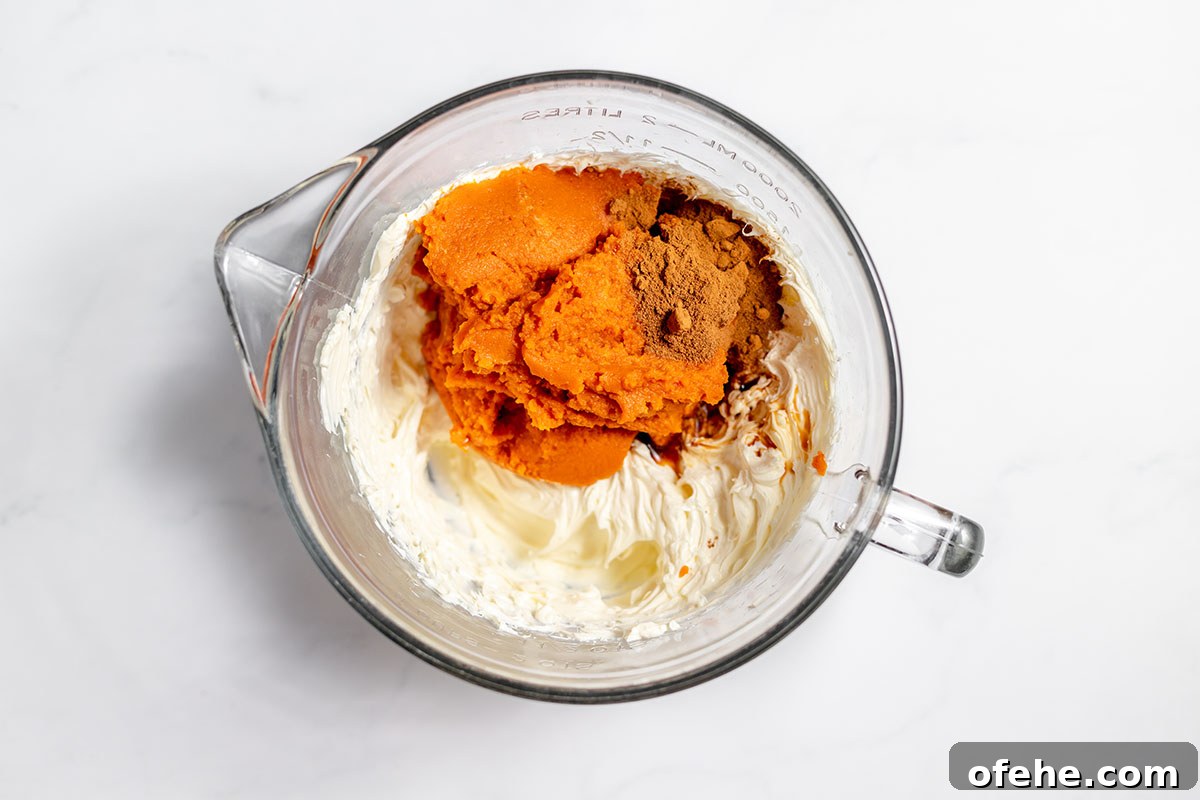 Pumpkin puree, ground cinnamon pumpkin pie spice, and powdered sugar are added to cream cheese in bowl.