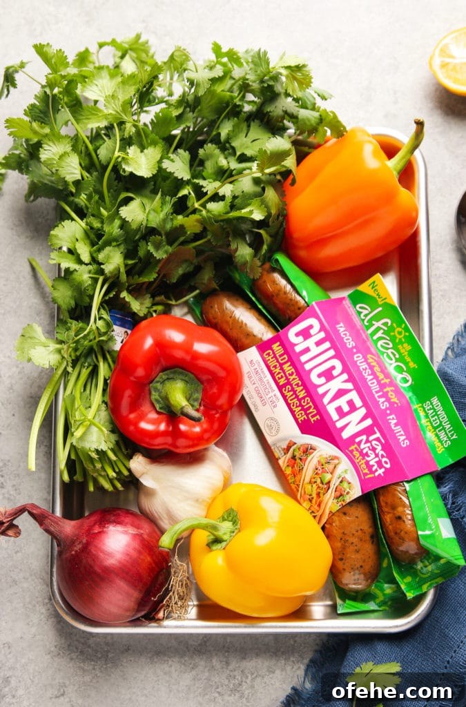 Parsley, bell peppers in orange, red and yellow, onion, garlic and chicken sausage in a large tray