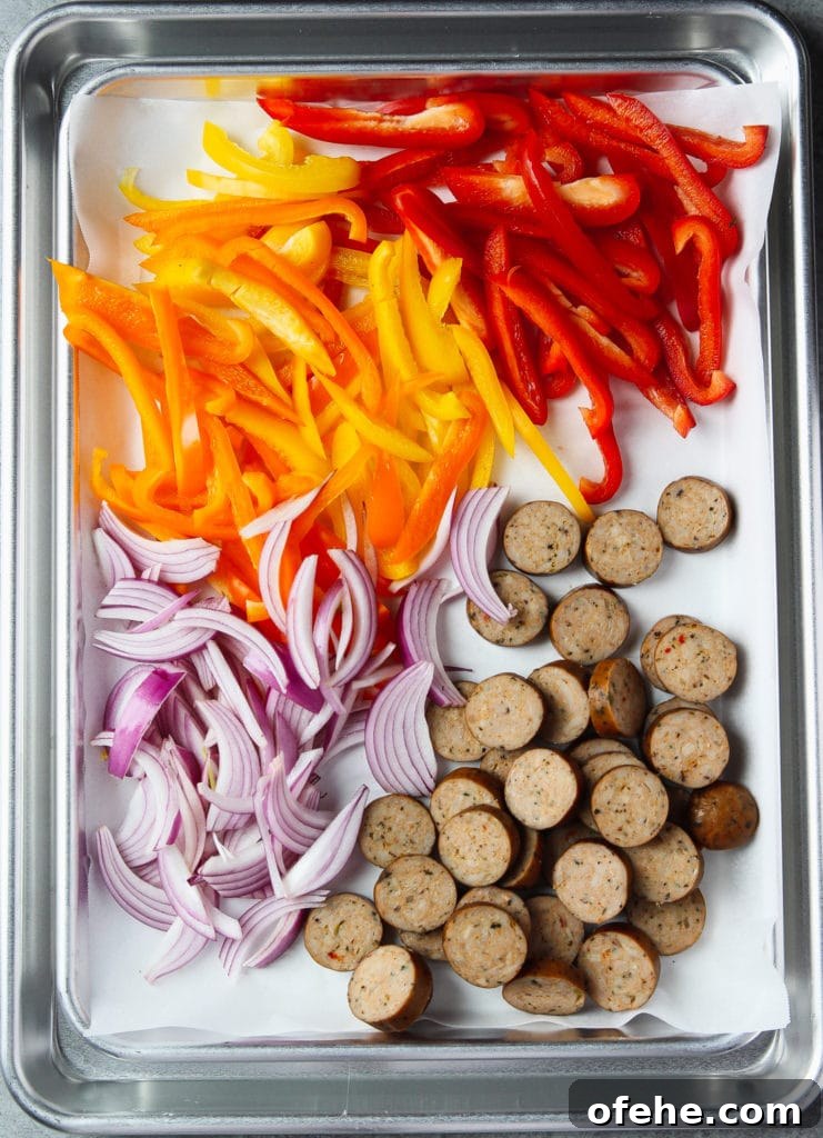 Bell peppers, onion and chicken sausages sliced arranged in a sheet pan lined with parchment paper