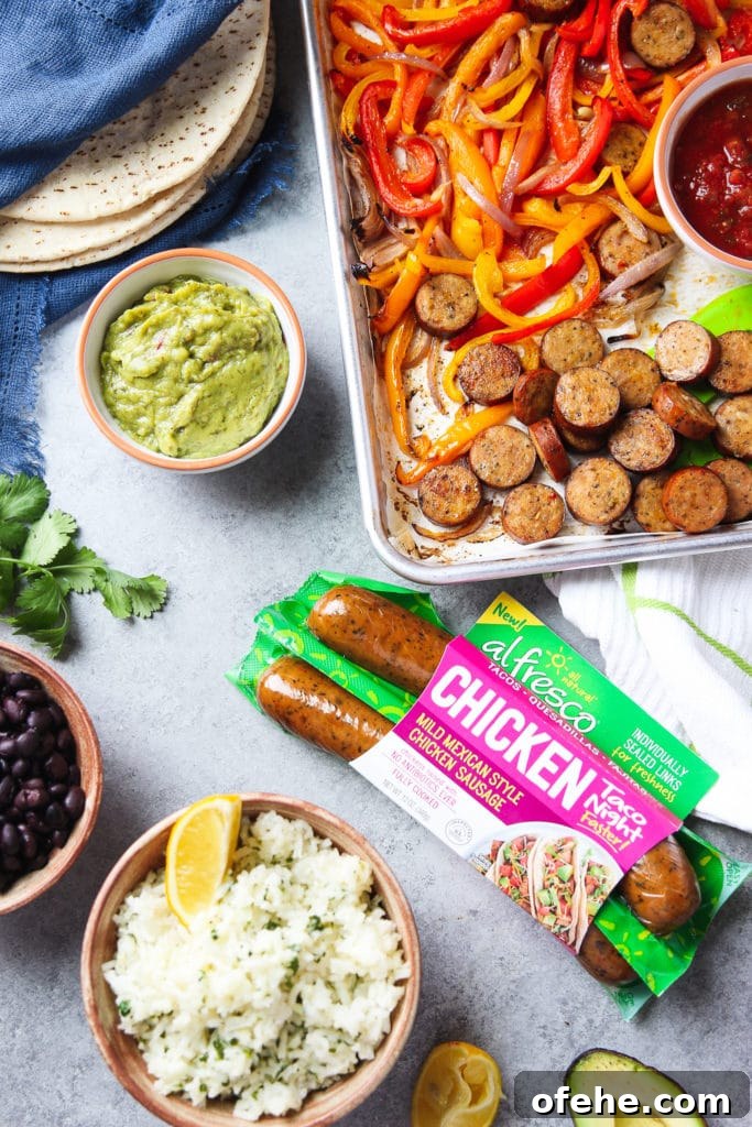 A sheet pan of chicken sausage fajitas surrounded by flat bread, a bowl of guacamole, a bowl or rice, a bowl of black beans, half a slice of avocado and some parsley
