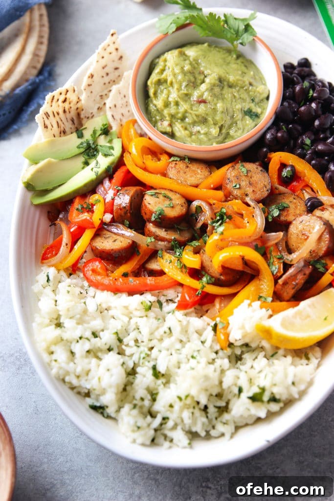 Sheet pan chicken sausage fajitas served in an oval-shaped bowl with rice, beans, slices of avocado, flat bread and a small bowl of guacamole