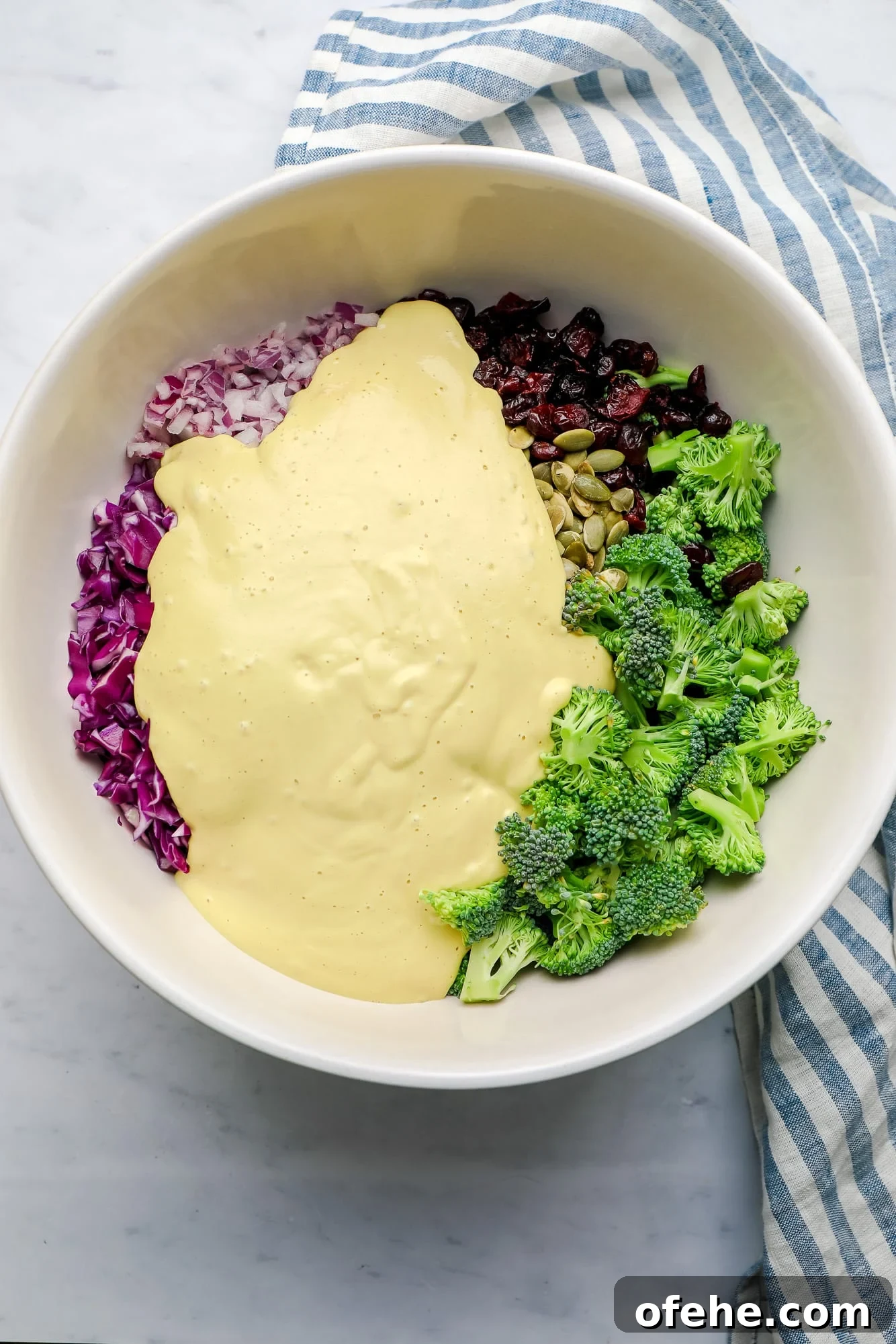 Vegan Broccoli Salad with Creamy Cashew Dressing 6 the ingredients for vegan broccoli salad with yellow creamy dressing poured on top in a large white bowl.