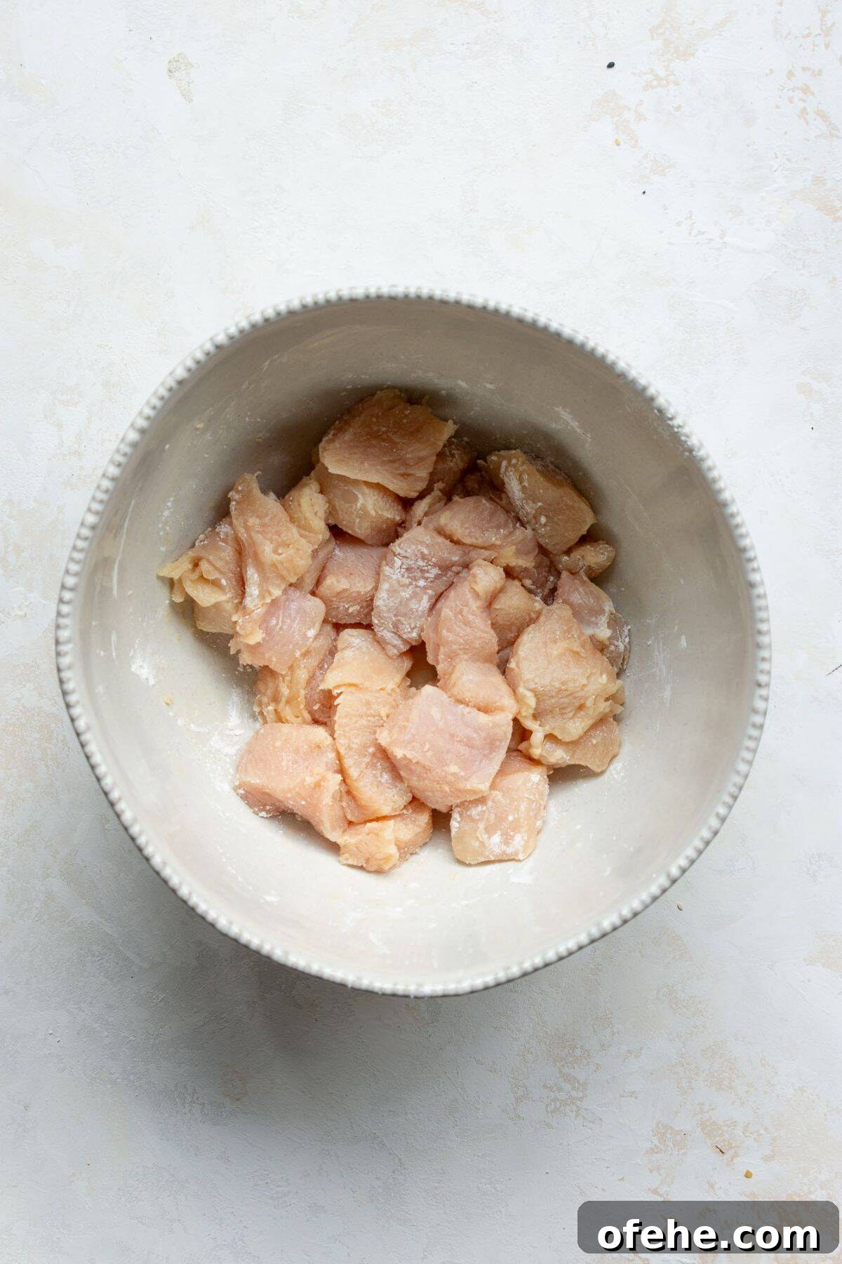 Crispy Sticky Air Fryer Teriyaki Chicken 5 Bite-sized chicken breast pieces in a bowl coated with arrowroot starch before air frying.