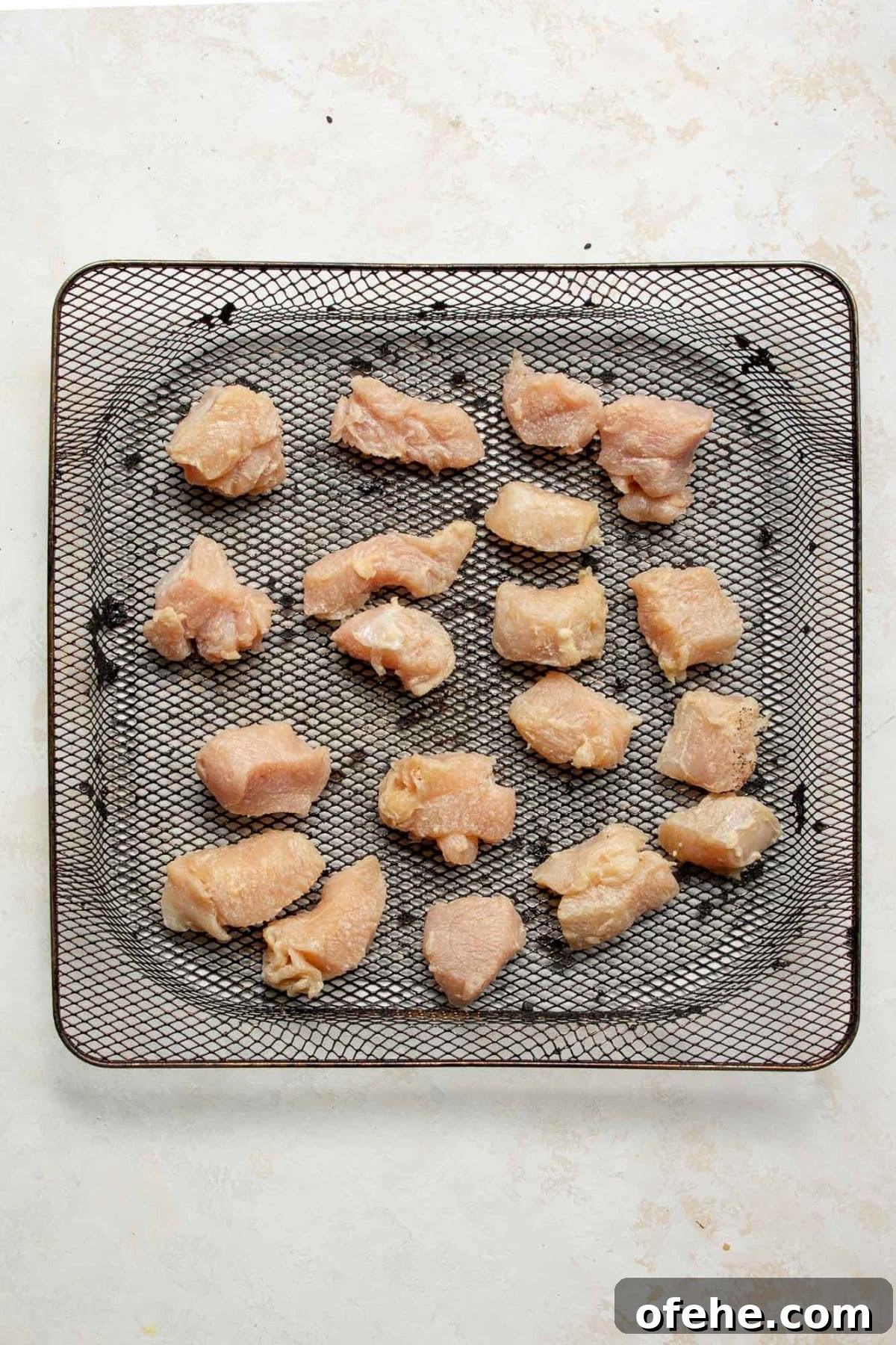 Crispy Sticky Air Fryer Teriyaki Chicken 6 Raw chicken breast bites arranged in an air fryer basket before cooking.