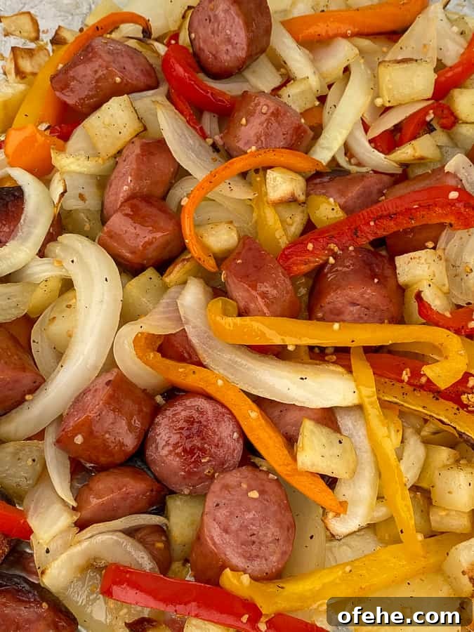 Pile of baked smoked sausage, onions, potatoes and orange, red and yellow bell pepper strips