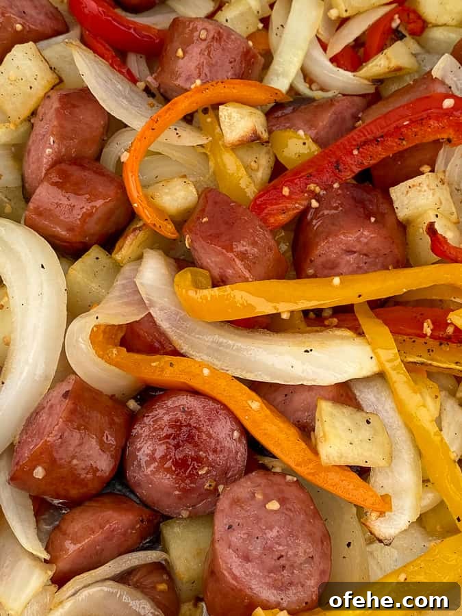 Close up roasted smoked sausage, cubes of potatoes and slices of bell peppers and onions