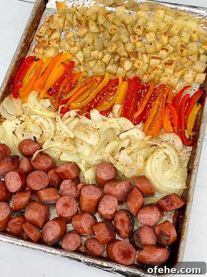 Rows of potatoes, peppers, onions and smoked sausage coins on sheet pan meal