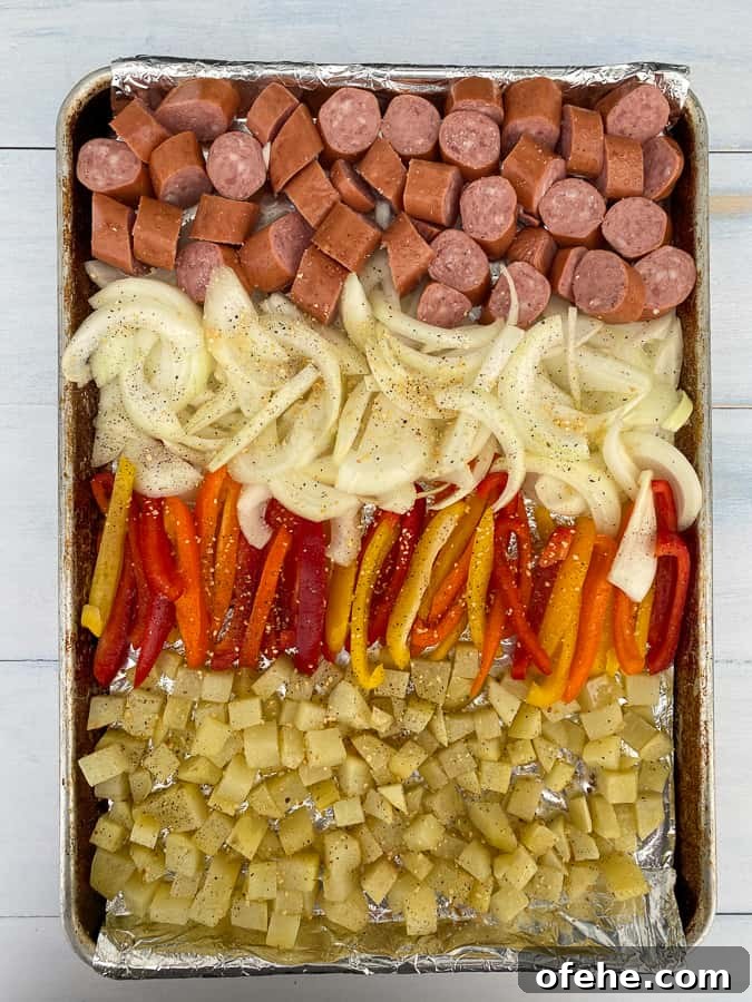 smoked sausage and vegetables along with potatoes on a foil covered sheet pan