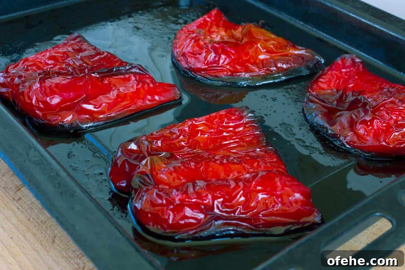 four havles of roasted red peppers on a black baking sheet