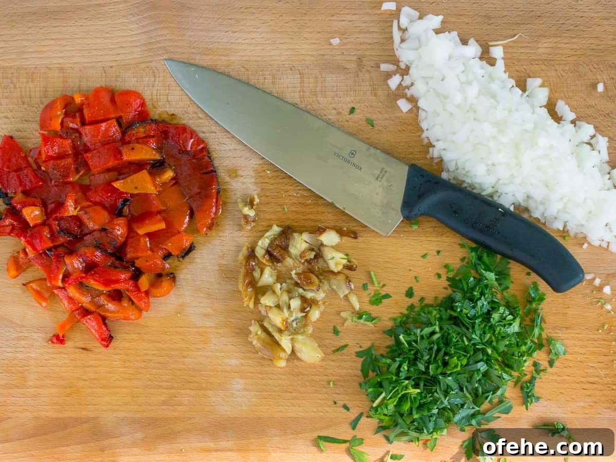 wooden cutting board, knife, chopped onion, roasted garlic and red pepper, and parsley