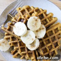 Overhead view of pumpkin waffles on gray plate topped with banana slices, cinnamon sprinkles, and syrup