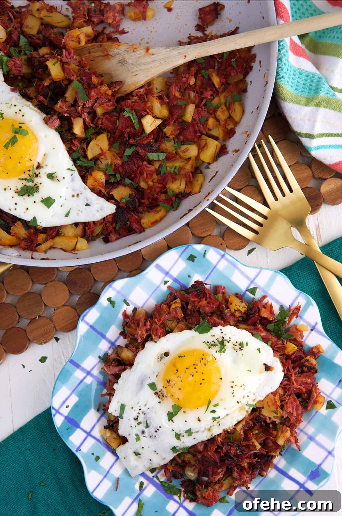 An egg is placed on top of a serving of hash next to a skillet filled with more hash.