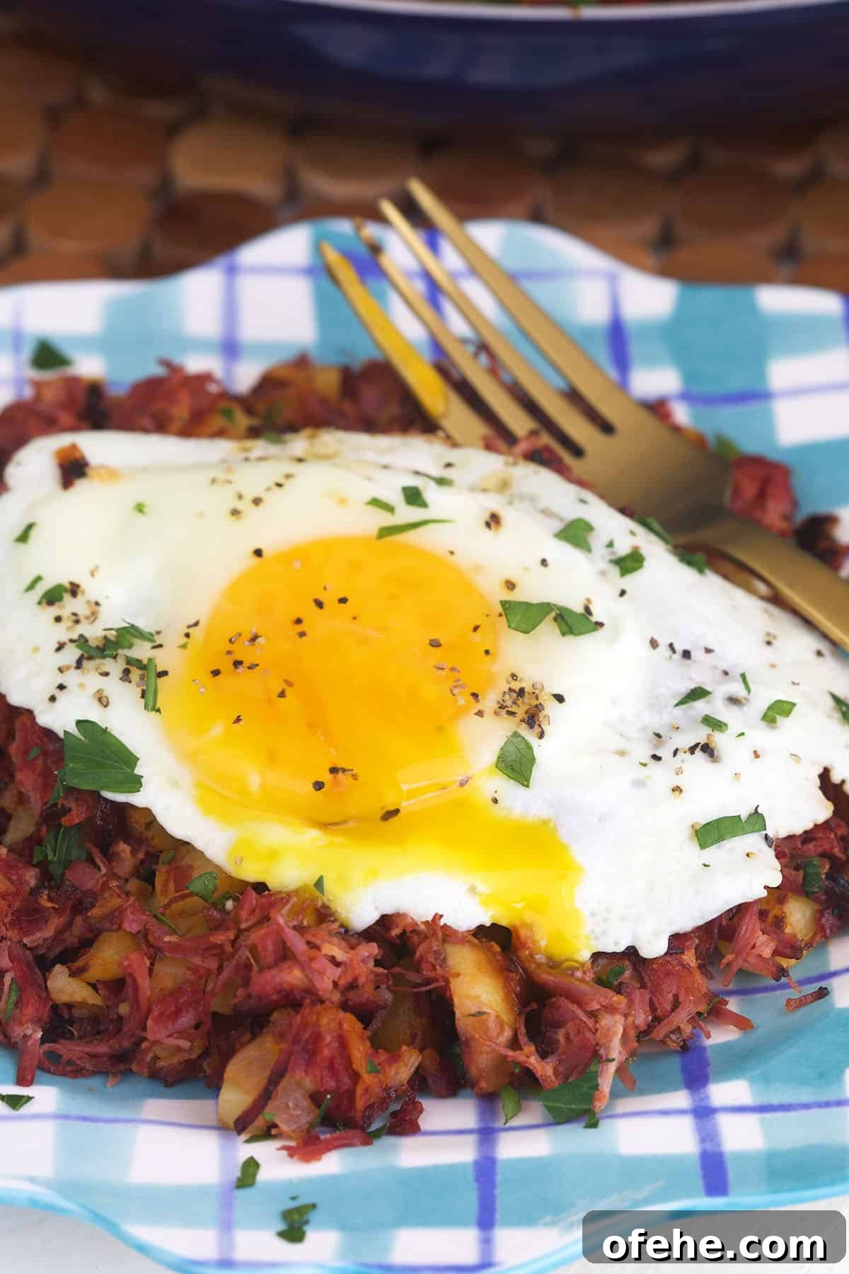 A fried egg is placed on top of hash next to a fork on a plate.