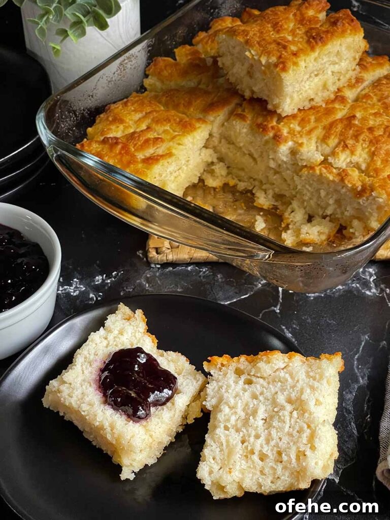 Butter swim biscuit cut in half with blackberry jam on one side on a black plate.