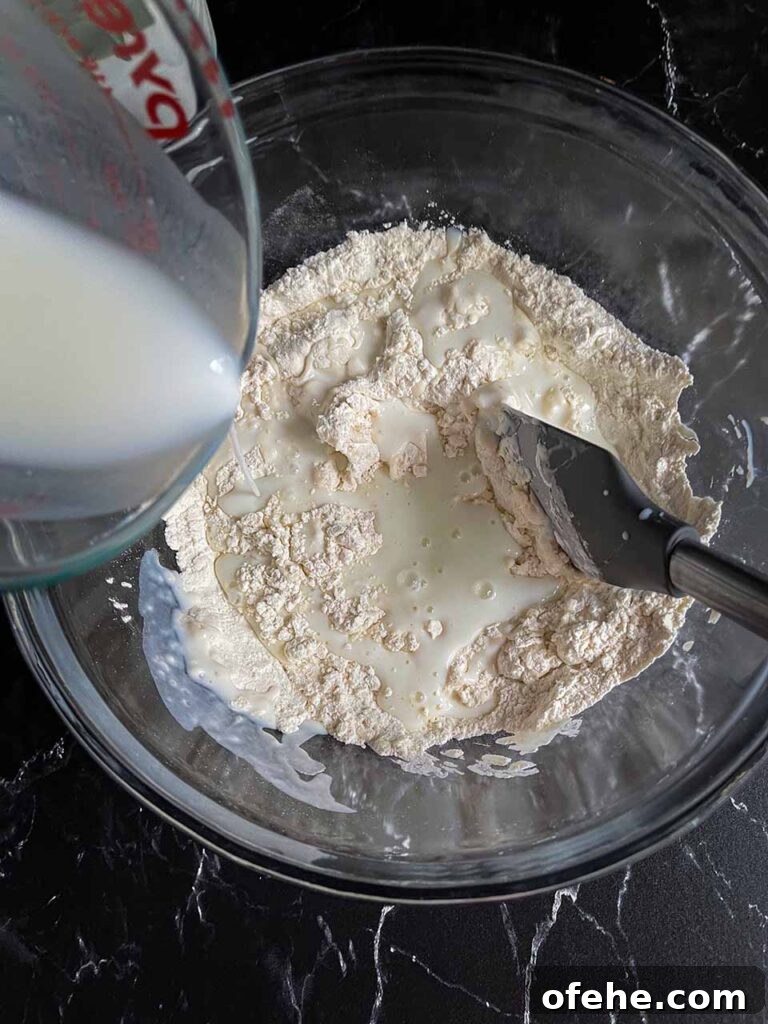 Buttermilk being stirred into the dry ingredients in a glass mixing bowl.