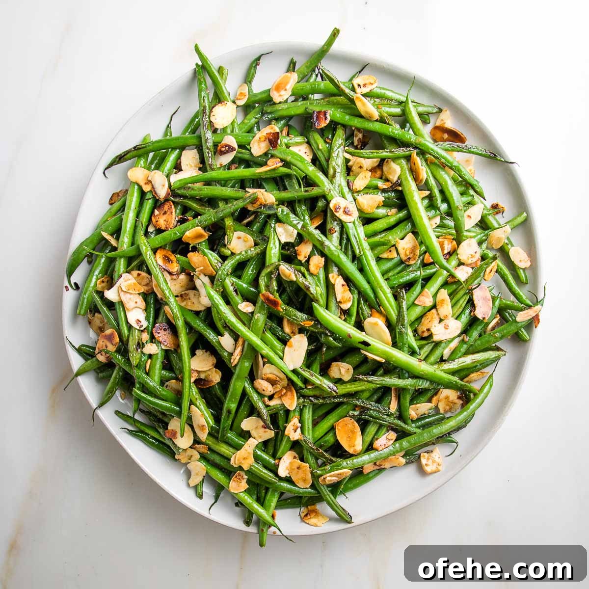 Wholesome Thanksgiving Recipes 2025 for a Lighter Feast 9 White plate with rim, filled with french cut green beans already cooked with sliced almonds.