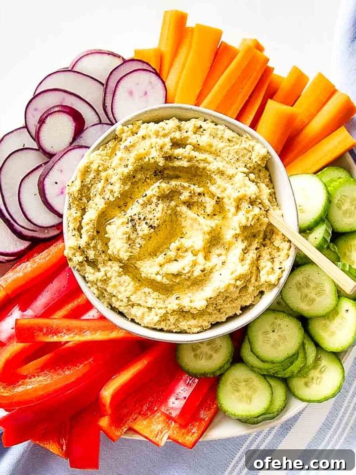 Bowl of hummus surrounded by colorful sliced veggies.
