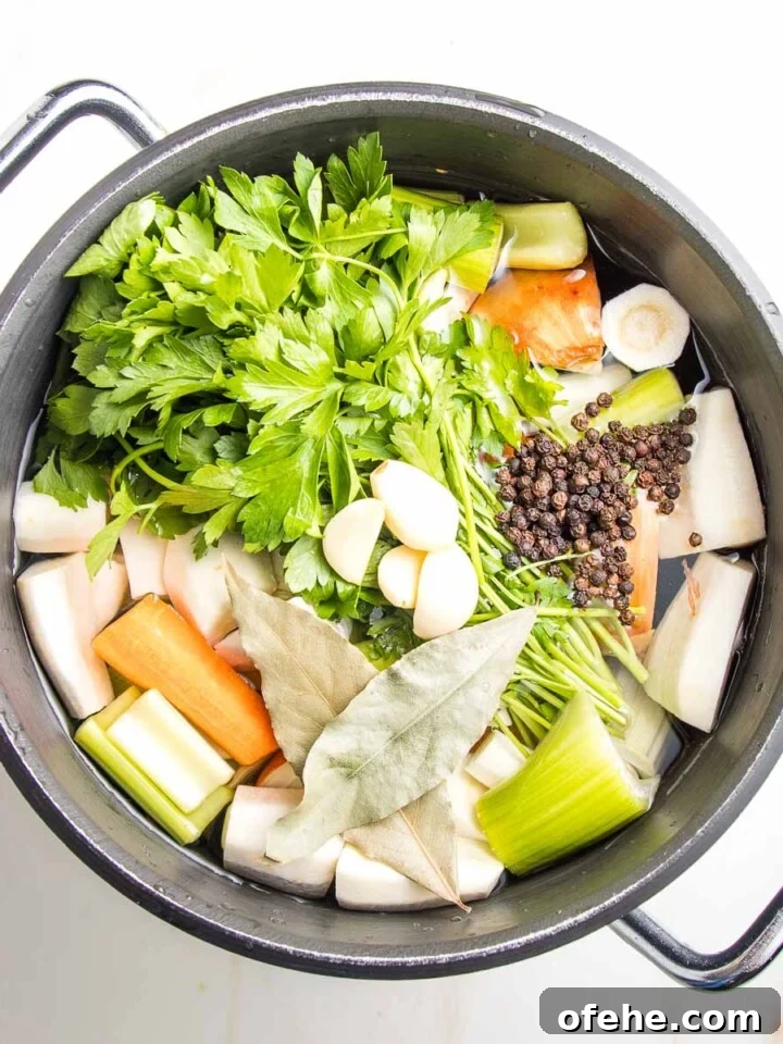 Stock pot filled with water and veggies: a bunch of parsley, carrots, onions, celery, parsnips, bay leaves and whole peppercorns.