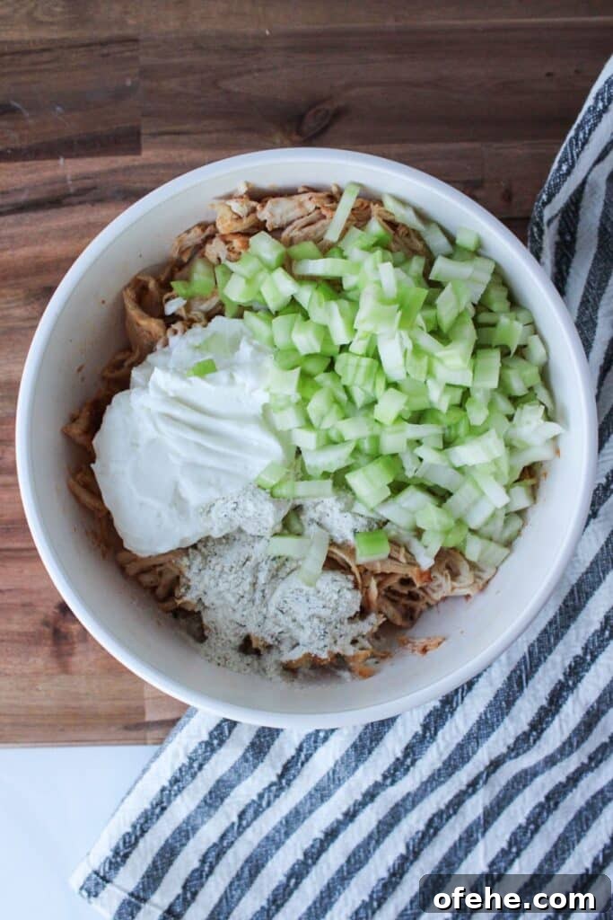 Shredded chicken, plain Greek yogurt, celery and ranch seasoning powder in a white bowl.