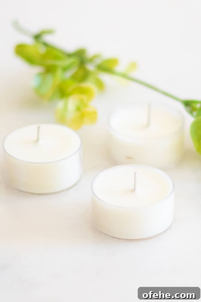 DIY Citronella Candles to Keep Mosquitoes Away 3 Homemade white citronella candles on white marble with greenery in background.